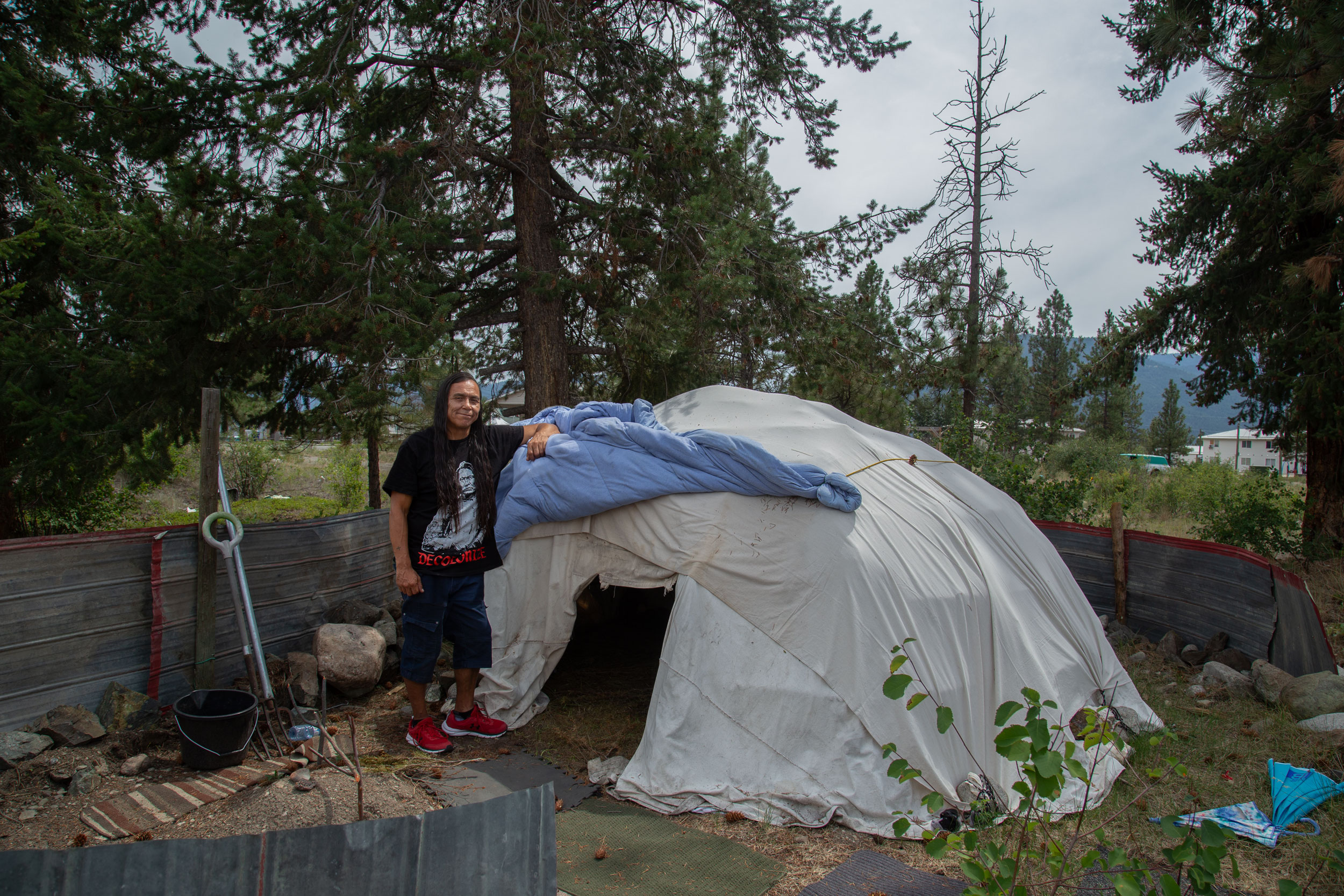 Indigener Mann aus Kanada lehnt an einem weißen Zelt.